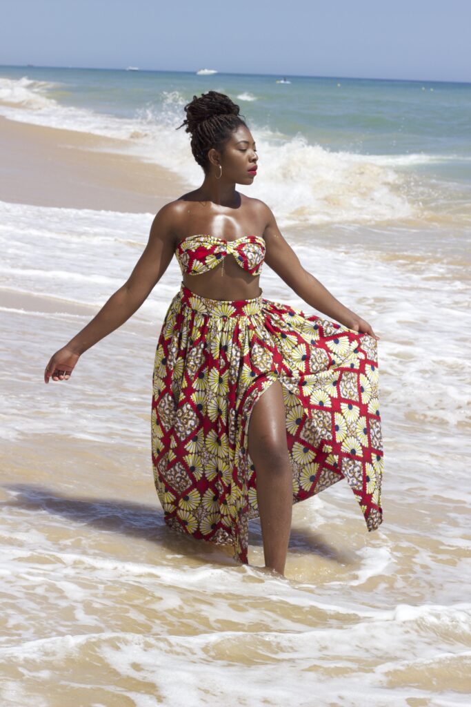 Metiya turning on the beach in vibrant two piece outfit and glowing skin with waves behind looking like freedom.
